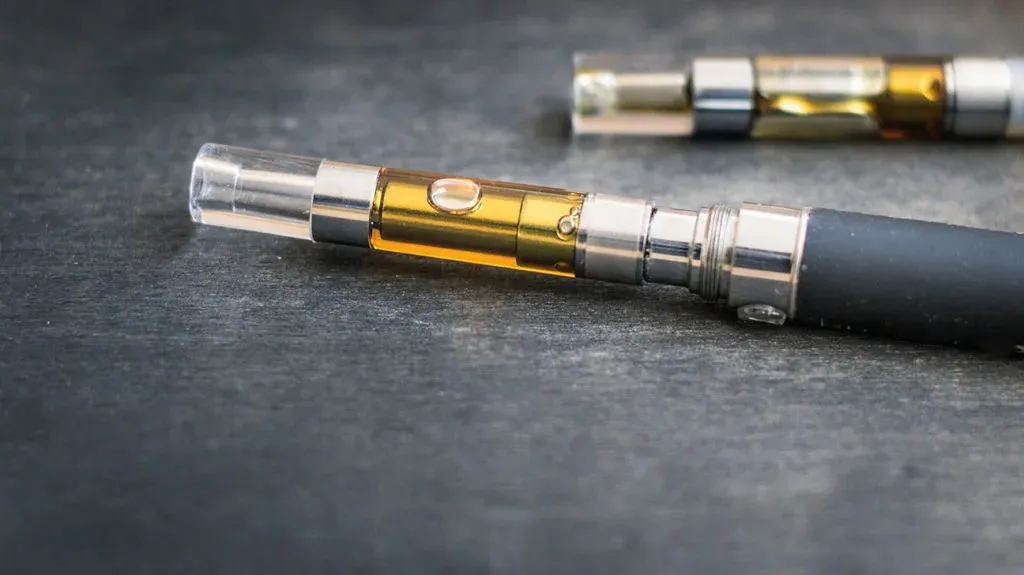 Close-up of a nicotine vape device producing vapor with e-liquid and battery components visible